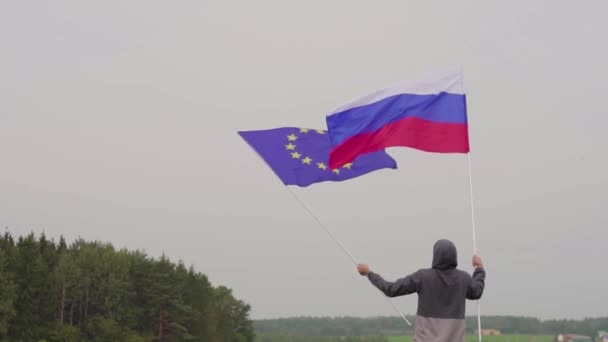 ВИДЕО. Человек с флагами Европейского Союза и России у пейзажа страны. Концепция дружбы и примирения . — стоковое видео