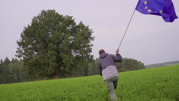 Man loopt met een vlag van de Europese Unie in landschappen. Standaard aan toonder — Stockvideo