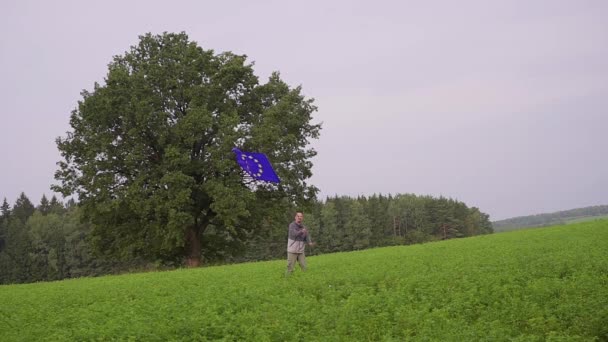 El hombre corre con una bandera de la Unión Europea en el paisaje del país. Portador estándar — Vídeo de stock