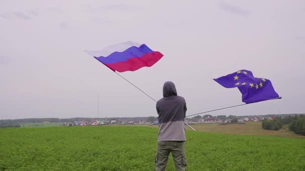 Video. man is wuivende vlaggen van de Europese Unie en Rusland op land landschap. Het concept van vriendschap en verzoening. — Stockvideo