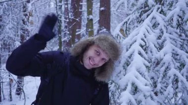Mutlu bir adam kameraya elini sallayarak soğuk kış orman içeri girer. karla kaplı.