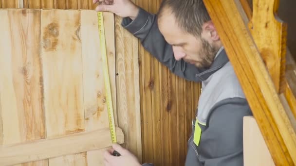 Der Arbeiter stellt eine selbstgebaute Tür in ein hölzernes Innere — Stockvideo