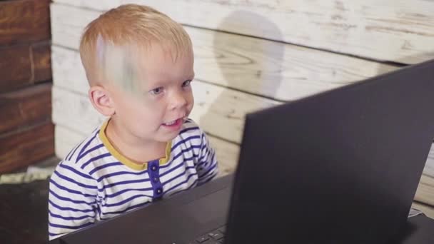 Rapaz de dois anos com um computador e dinheiro a cair. menino sorrindo sentado à mesa com laptop e notas de dólar no ar. Conceito de negócio bem sucedido. câmara lenta — Vídeo de Stock