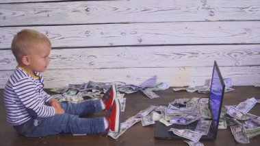bir bilgisayar ve düşen para ile iki yaşında bir çocuk. dizüstü bilgisayar ve doları banknot hava ile masada oturan boy gülümseyerek. Başarılı iş kavramı