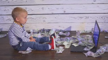 bir bilgisayar ve düşen para ile iki yaşında bir çocuk. dizüstü bilgisayar ve doları banknot hava ile masada oturan boy gülümseyerek. Başarılı iş kavramı