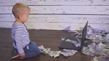bir bilgisayar ve düşen para ile iki yaşında bir çocuk. dizüstü bilgisayar ve doları banknot hava ile masada oturan boy gülümseyerek. Başarılı iş kavramı