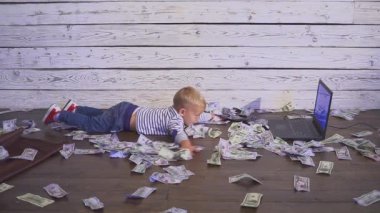 bir bilgisayar ve para ile iki yaşında bir çocuk. dizüstü bilgisayar ve doları banknot ile masada oturan boy gülümseyerek. Başarılı iş kavramı