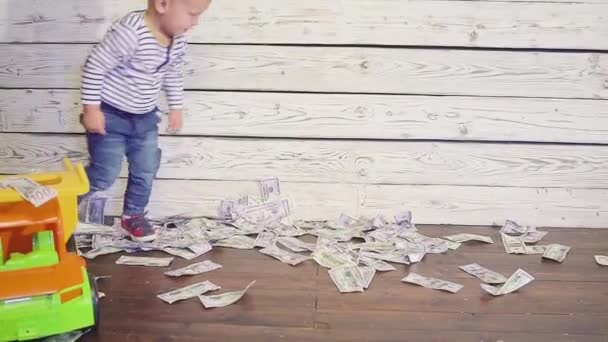 Το αγόρι παίζεται με ένα αυτοκίνητο παιχνίδι στο πάτωμα, όπου πολλά χρήματα. έννοια του πλούτου — Αρχείο Βίντεο
