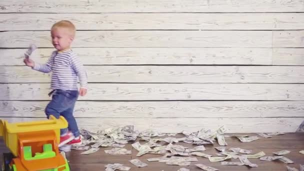 The boy is played with a toy car on the floor, where a lot of money. concept of wealth — Stock Video