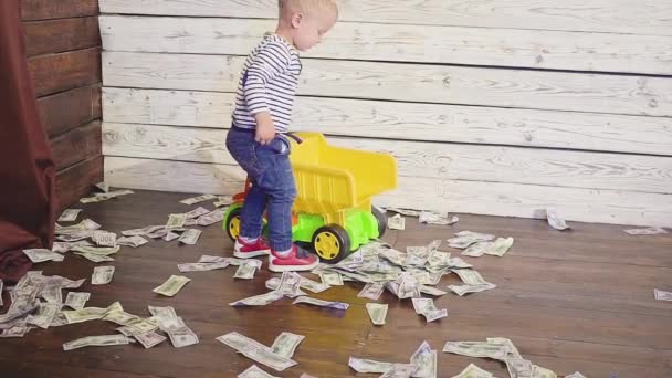 这个男孩在地板上玩玩具车, 那里有很多钱。财富概念 — 图库视频影像