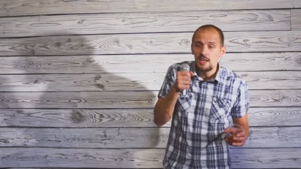 П'яний чоловік тримає келих алкоголю і співає на мікрофоні на вечірці — стокове відео