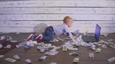 bir bilgisayar ve para ile iki yaşında bir çocuk. dizüstü bilgisayar ve doları banknot ile masada oturan boy gülümseyerek. Başarılı iş kavramı