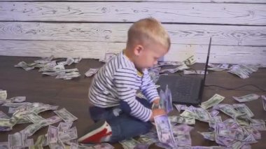 bir bilgisayar ve para ile iki yaşında bir çocuk. dizüstü bilgisayar ve doları banknot ile masada oturan boy gülümseyerek. Başarılı iş kavramı