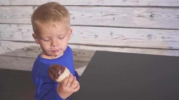 Το αγόρι τρώει παγωτό, κάθεται σε μια καρέκλα. χαριτωμένο παιδί απολαμβάνοντας ένα δροσιστικό παγωτό σε κώνο βάφλα. κοιτάζει προς. — Αρχείο Βίντεο