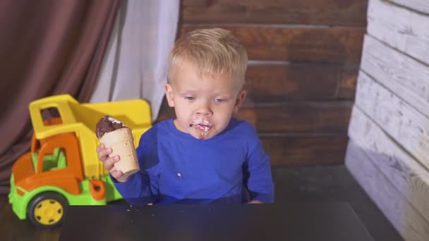 Pojken äter glass som sitter i en barnstol. söta barn som njuter av en glass i en våffla kon. ser mot. — Stockvideo