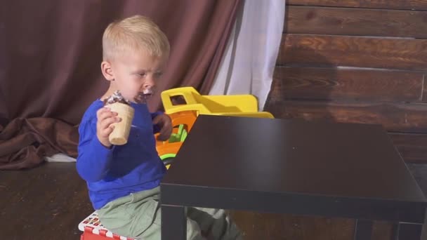 Ragazzo mangiare gelato seduto su un seggiolone. carino bambino godendo di un gelato in un cono di cialda. guarda verso . — Video Stock