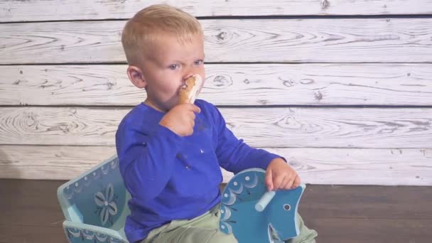 吃冰淇淋的男孩坐在一张高椅子上。可爱的孩子喜欢在华夫饼锥冰淇淋。看向. — 图库视频影像