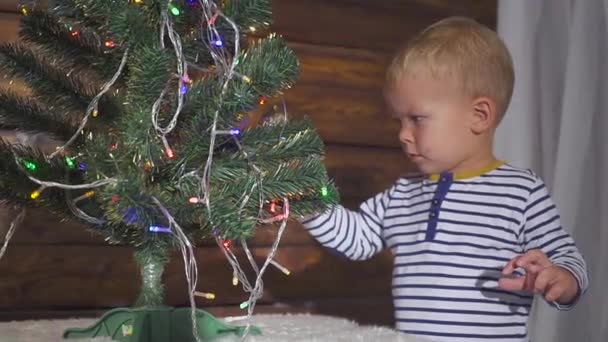 Two year old boy playing with Christmas toys on Christmas tree, close up. Portrait of a child near a Christmas tree. — Stock Video