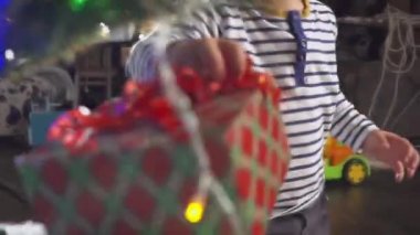 diğer bir sürü hediye kutuları ile bir Noel ağacı arkasında kırmızı kurdele ile bir hediye alma iki yaşındaki küçük tatlı çocuğa. Noel ağacı ışıkları ve altın top ile dekore edilmiştir. Tatil.
