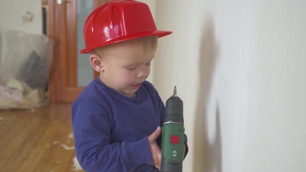 Ung söt builder pojke i uniform och hård hatt eller hjälm med elektrisk skruvmejsel mot bakgrund av byggande och reparation. — Stockvideo