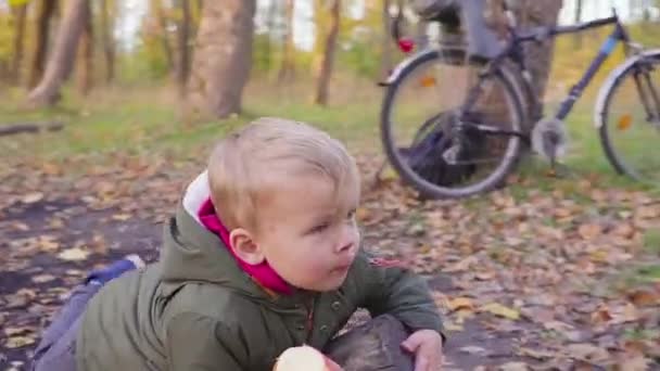 mignon petit bébé dans le parc d'automne avec des feuilles jaunes manger une pomme .