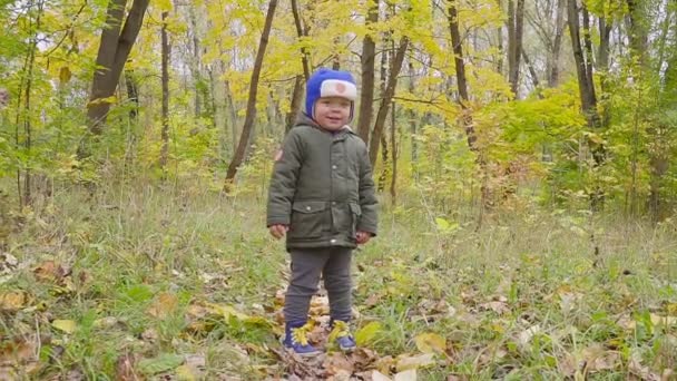 mignon bébé garçon dans une veste verte courir parmi les feuilles tombées dans le parc d'automne 