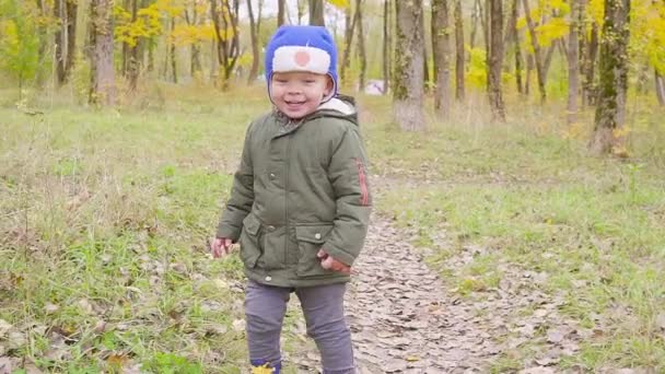 mignon bébé garçon dans une veste verte courir parmi les feuilles tombées dans le parc d'automne. gros plan .