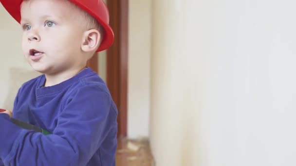 Jonge schattige bouwer jongen in uniform en harde hoed of helm met elektrische schroevendraaier tegen de achtergrond van de bouw en reparatie. — Stockvideo