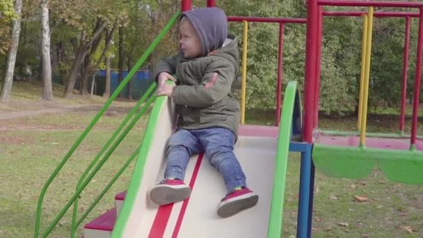 Fröhlicher Junge reitet auf Spielplatz den Hügel hinunter — Stockvideo