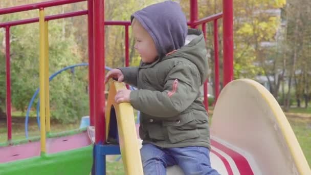 Веселый мальчик, скачущий с холма по детской площадке — стоковое видео