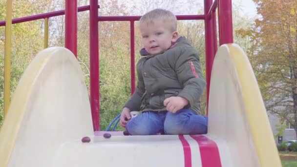 Веселий хлопчик їде по пагорбу на дитячому майданчику — стокове відео