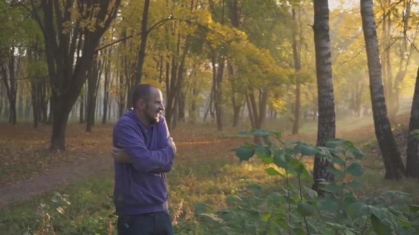 Knappe man gevoel koude en opwarming van de aarde handen, man bevriest in de herfst park. koud. — Stockvideo