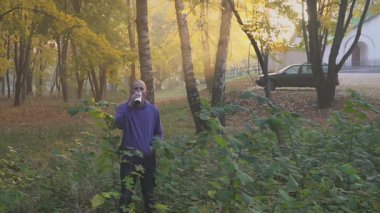 Genç adam bir thermocup Sonbahar Park çay veya kahve içme