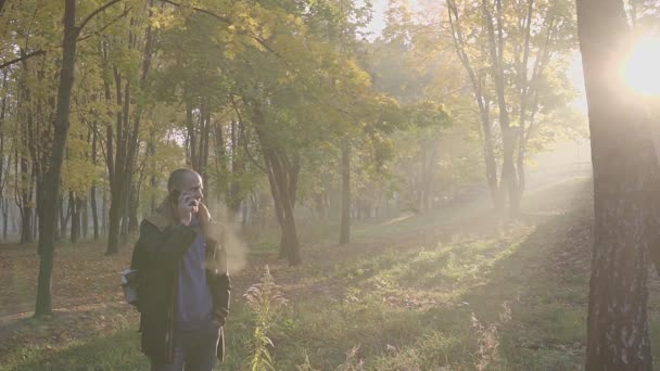 Szép szakállas fiatalember beszélő telefon mobil az őszi parkban — Stock videók