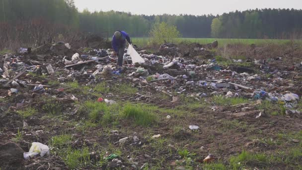 Bezdomny mężczyzna szuka przydatne przedmioty i żywność dla przeżycia między śmieci w wysypisko śmieci hałdy. Zanieczyszczenie środowiska. Ubóstwa. W torbie są puste butelki. — Wideo stockowe