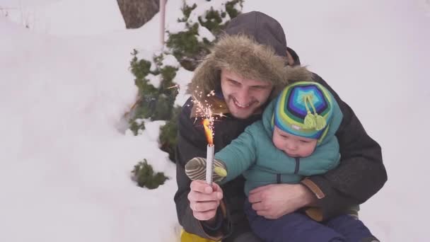 Padre, hijo y fuego de Bengala en el parque junto al árbol de Navidad. Preciosa familia celebrando la Navidad en casa — Vídeo de stock