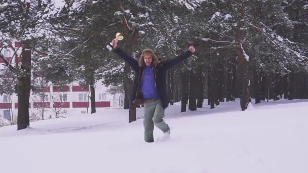 Homem feliz com um prêmio em suas mãos salta e se alegra na floresta de inverno. Vitória desportiva em competições. Movimento lento — Vídeo de Stock