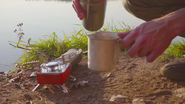 Mãos masculinas fazer comida ou bebida quente em um fogão a gás na floresta de outono perto do lago — Vídeo de Stock