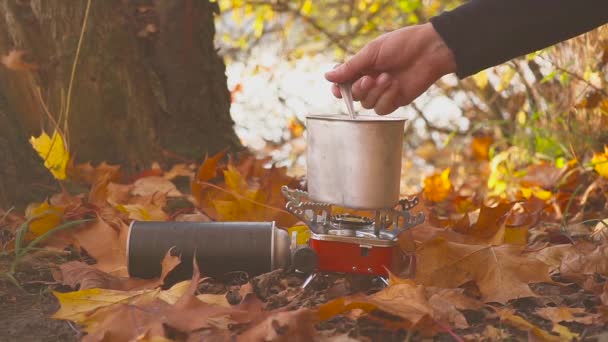 Manliga händer göra mat eller varm dryck på en gasspis i höst skogen nära sjön — Stockvideo