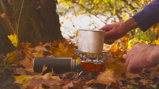 Mãos masculinas fazer comida ou bebida quente em um fogão a gás na floresta de outono perto do lago — Vídeo de Stock