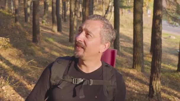Glimlachende Man toerist met een rugzak verheugt zich in de herfst bos — Stockvideo