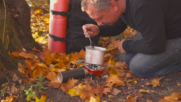 Kochen im Herbstwald auf einem Gasbrenner. der Tourist probiert das Essen aus dem Topf. — Stockvideo