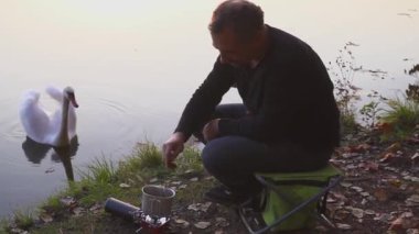 Kamp yemek yapma. Turistik kahve veya çay ya da gaz sobası yemek pişiriyor. Güzel manzara arka planda kuğu. Göl kıyısında yemek kamp kurup gıda deneyin.