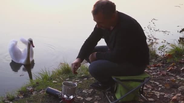 Kamp yemek yapma. Turistik kahve veya çay ya da gaz sobası yemek pişiriyor. Güzel manzara arka planda kuğu. Göl kıyısında yemek kamp kurup gıda deneyin. — Stok video