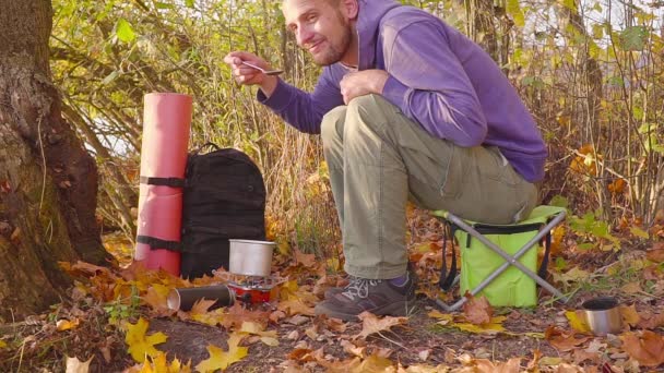 Cocinar en el bosque de otoño en un quemador de gas. El turista prueba la comida de la olla . — Vídeo de stock