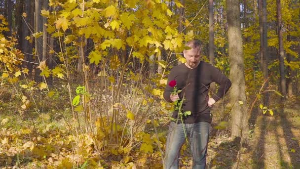 Hombre con rosas rojas esperando a su amada mujer en una cita en el bosque de otoño — Vídeo de stock
