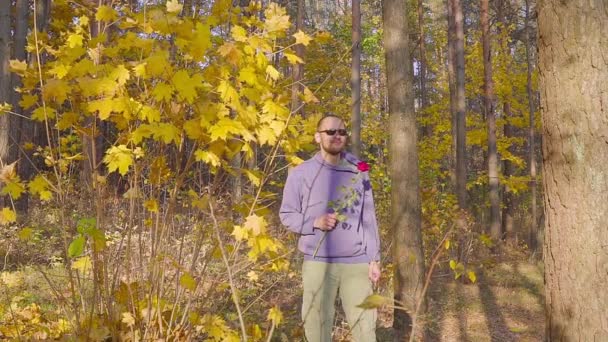 Mann mit roten Rosen wartet auf seine geliebte Frau bei einem Date im Herbstwald — Stockvideo