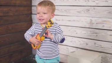 Mutlu bir çocuk gitar ya da ukulele çalar ve ahşap odada oturup şarkılar söyler..