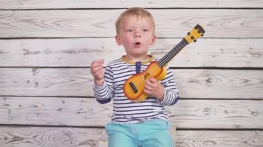 Bir yıl yaşlı erkek çocuk onun gitar ya da gitar çalıyor ve ahşap odada oturmuş şarkı söylüyor.