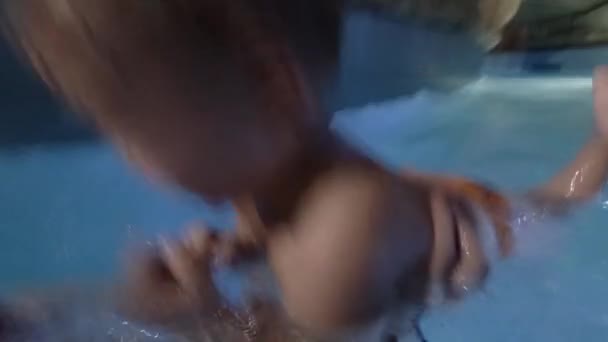 Feliz joven madre sosteniendo al bebé en brazos, sonriendo y jugando con él en la piscina . — Vídeo de stock